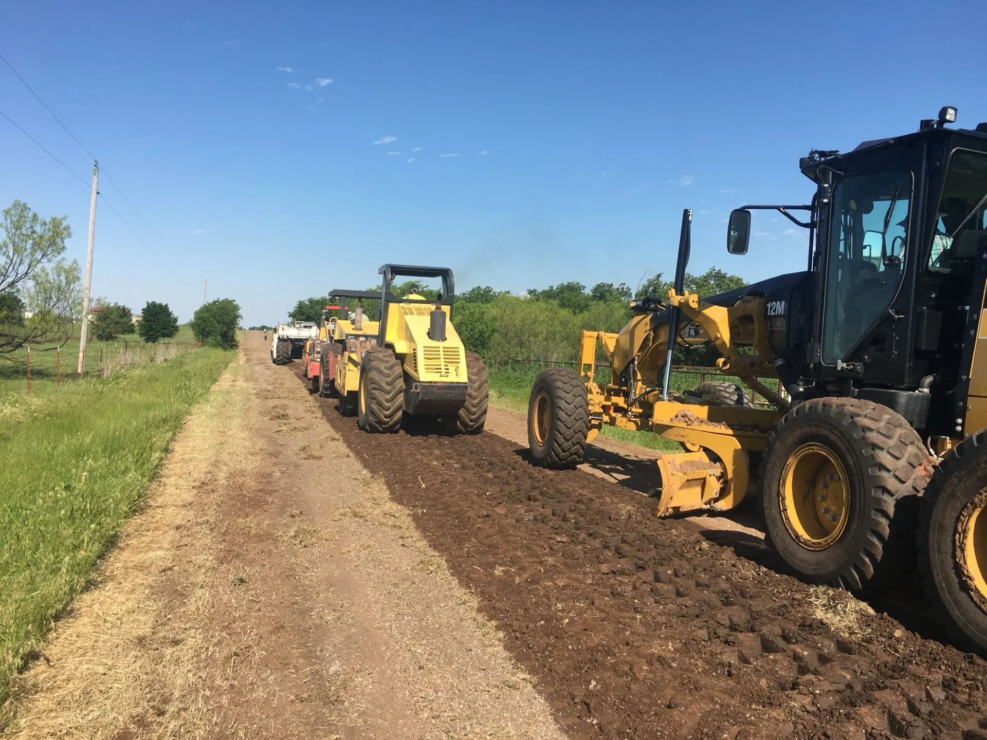 Graders, rollers and a reclaimer working in a line along a treated county road