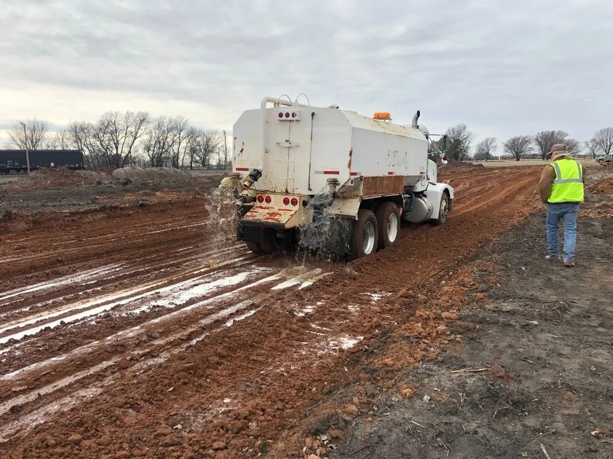 Water truck applying stabilizer solution across a tilled clay site